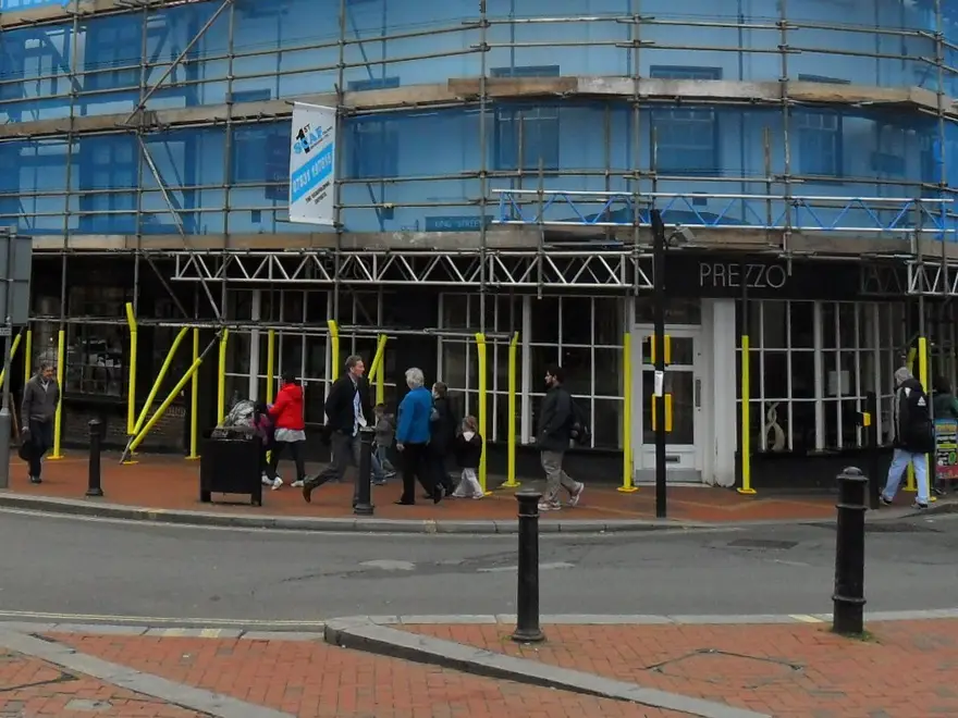 Lattice beams carrying the scaffold over shopfronts at The George Hotel, Reading, with pedestrians walking beneath